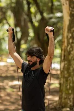 Strong man guy working out with elastic rubber bands at a park outdoors. Athl Stock Photos
