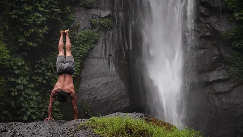 Strong man handstanding in front of waterfall Stock Footage 274250336
