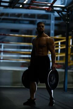 Strong man lifts weights in training area during evening workout session Stock Photos