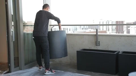 Strong man places large black decorative containers on balcony. Stock Footage 88522011