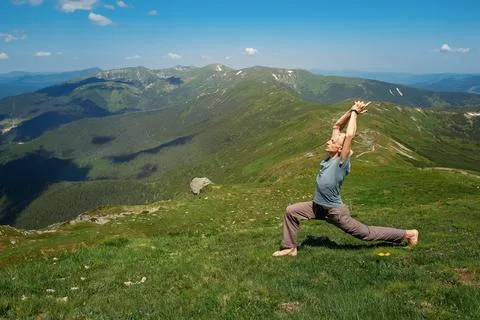 Strong man practicing yoga exercises under sky on mountain top Stock Photos