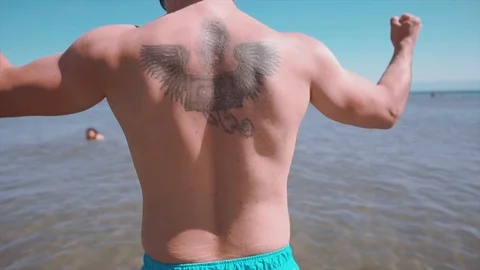 Strong man showing his back muscles on sea, beach in summer time. Stock Footage 112288662