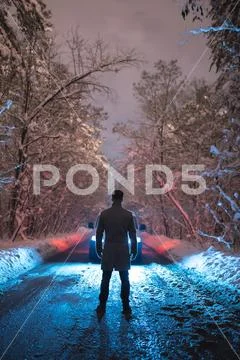 The strong man stand near the car on the snowy road. evening night time Stock Photos