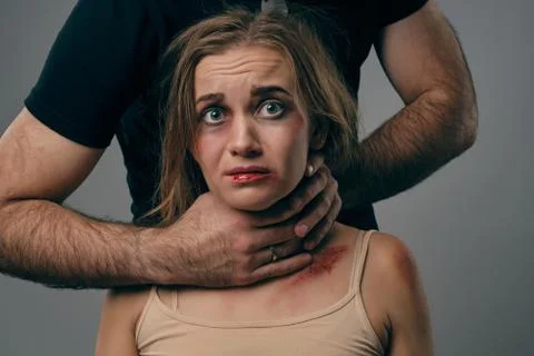 Strong man is strangling scared blonde female with bruises on her face. Posing Stock Photos