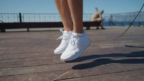 Strong man is training alone near sea, jumping rope. Closeup of male feet 스톡 동영상 199689563