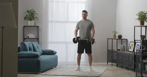 Strong man is training at home during self-isolation, lifting dumbbells Stock Footage 147933502