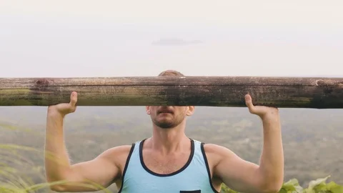 Strong man training press exercise with wooden barbell on tropical hill Stock Footage 107138189