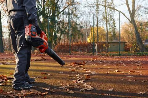 Strong man working with leaf blower at outdoors tennis court. Stock Photos