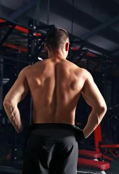 Strong masculine man athlete doing standing in dark fitness club background.  Stock Photos