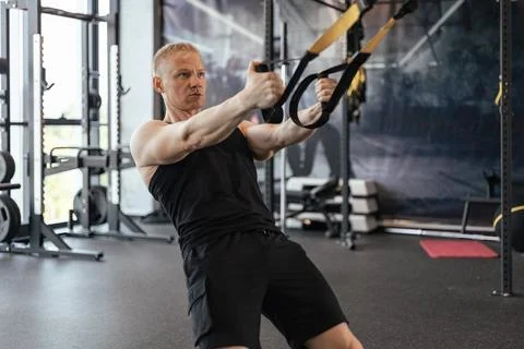 Strong middle-aged man doing push ups with TRX in the gym. Stock Photos