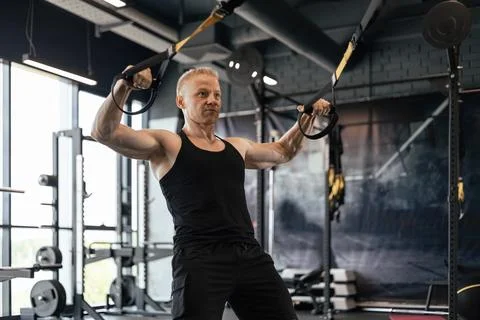 Strong middle-aged man doing push ups with TRX in the gym. Stock Photos