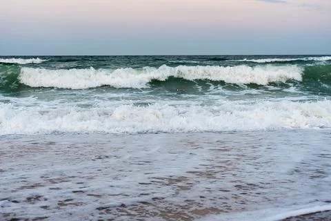 Strong ocean waves breaking on sandy beach at sunset Stock Photos