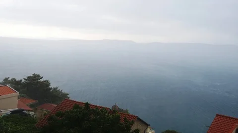 Strong rain in the summer, shot of the roofs of houses and sea Stock Footage 96160928
