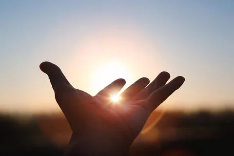 Strong rays of light shining between hands stretched out toward the sunrise sun Stock Photos