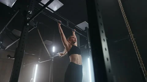 Strong sportswoman is doing pull-ups in gym, training alone in evening in dark Video stock 171180798