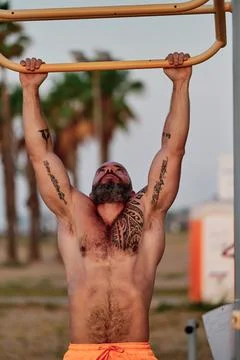 Strong sporty man doing pull-ups exercise during workout outdoors. Stock Photos