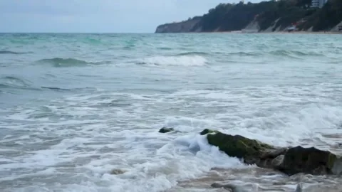 Strong waves break against rocks. Foamy sea waves arrive at the sandy seashore Stock Footage 315177279