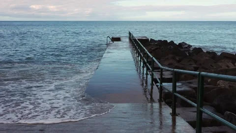 Strong waves repeatedly strike a concrete pier, creating bursts of white foam Stock Footage 346890253