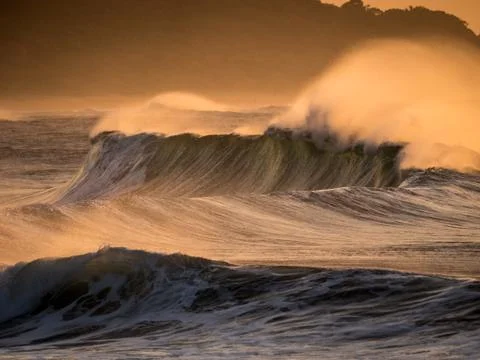 Strong wind blows sea spray off the tops of large powerful breaking Stock Photos