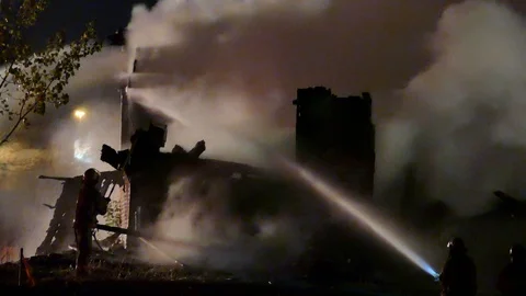 Strong winds push smoke from a structure fire at night with firemen Stock Footage 115016435