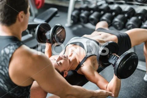 Strong woman with barbells exercising with trainer near by Stock Photos