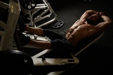 Strong young bearded male lying in exercise machine during pause in heavy spo Stock Photos