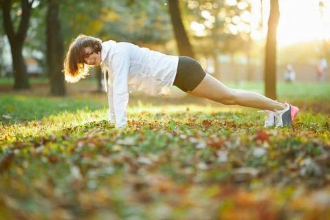 Strong young lady doing plank exercise at sunny park Stock Photos