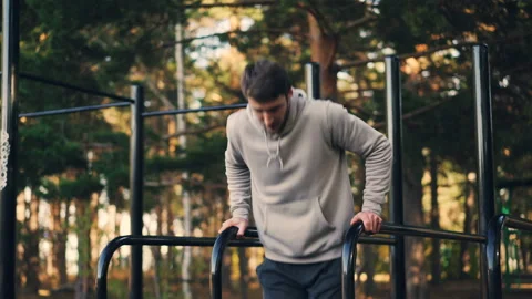 Strong young man is doing triceps dips on parallel bars in city park exercising 動画素材 98919939