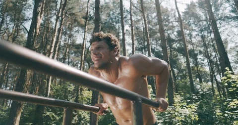 Strong young man is doing triceps dips on parallel bars. Exercising outdoors in 動画素材 114240421