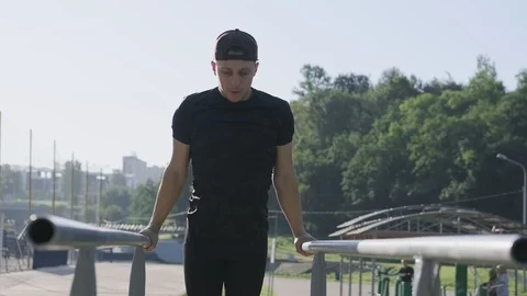 Strong young man doing triceps dips on parallel bars at sunny morning Stock Footage 115022797