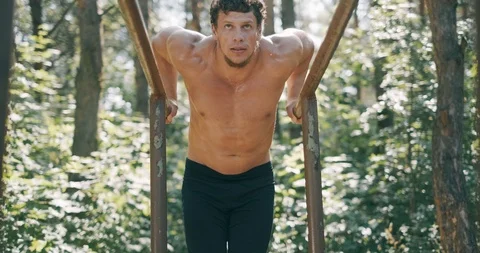 Strong young man is doing triceps dips on parallel bars. Exercising outdoors in Stock Footage 116772631