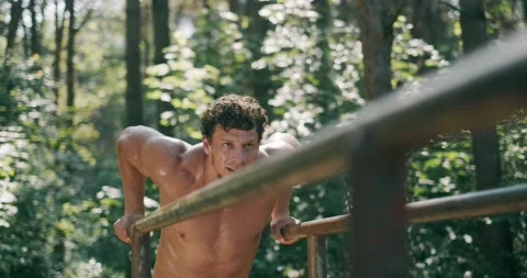 Strong young man is doing triceps dips on parallel bars. Exercising outdoors in 動画素材 132296935