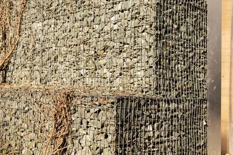 A structure built from stones held together by wire is seen outdoors. Sunli.. 库存照片