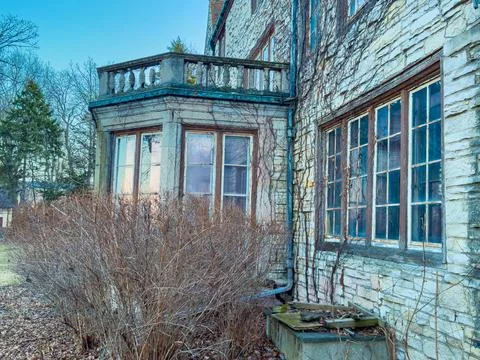 A structure with stone walls has multiple windows. It is located in a rural a Stock Photos