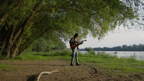 Strumming man guitar by the riverside at sunset Stock Footage 319947201