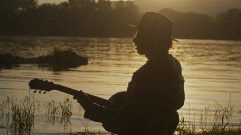 Strumming silhouette man by the river during sunset Stock Footage 319952630
