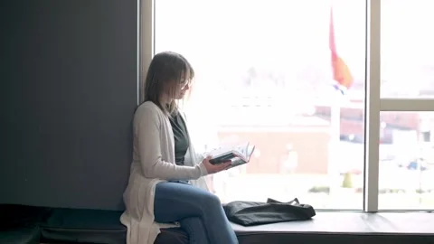 Student absorbed in her book while seated by a large window in a university l Stockbeeldmateriaal 274516786