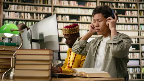 Student adjusting headphones at library study desk with computer Stock Footage 337228795