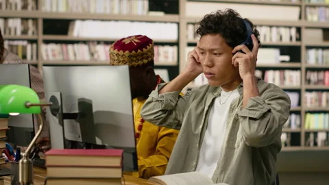 Student adjusting headphones at library study desk with computer Stock Footage 337230692
