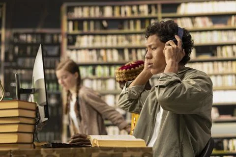 Student adjusting headphones at library study desk with computer Stock Photos