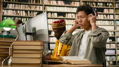 Student adjusting headphones at library study desk with computer Stock Photos