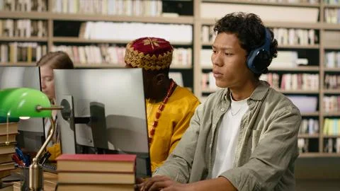Student adjusting headphones at library study desk with computer Stock Photos