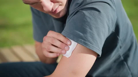 Student applying nicotine patch on upper arm with soft sunlight and blurred Stock Footage 307055698