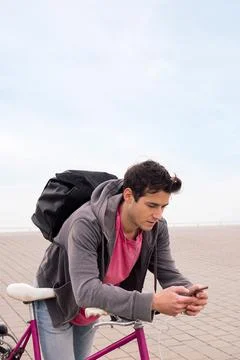 Student with backpack leaning on bike using phone Foto stock