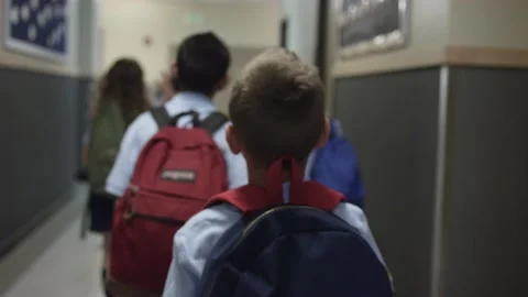 Student with backpack on walks down hallway at school. Over the shoulder shot. Stock Footage 139655853