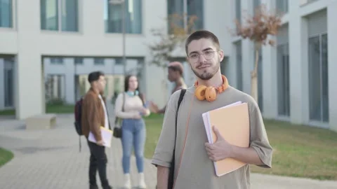 Student boy looking at camera while his friends are behind talk in university Stock Footage 222741989