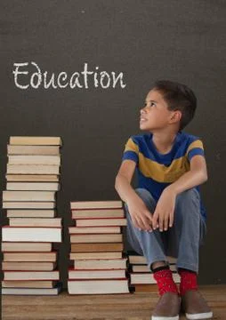 Student boy sitting on table against grey blackboard with education text Foto stock
