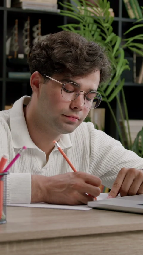 Student boy studying in a modern library. Young man with glasses sitting at an Video stock 316607064