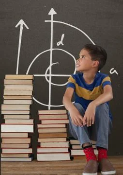 Student boy on a table looking up against grey blackboard with school and 스톡 사진