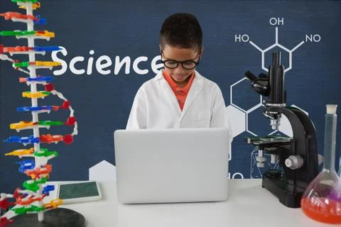 Student boy at table using a computer against blue blackboard with science text Stock Photos